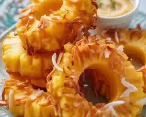 Crispy Fried Pineapple Rings: A Tropical Treat to Savor 3 Crispy fried pineapple rings with coconut coating, served with a creamy dipping sauce.