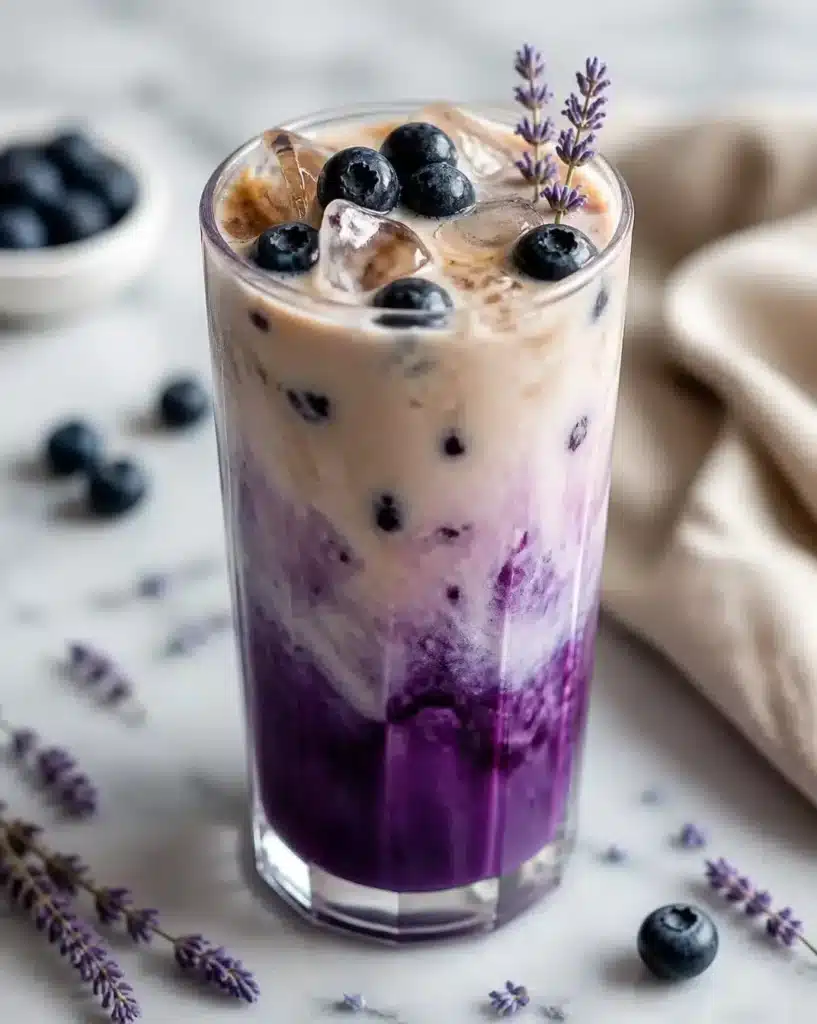Oat milk latte topped with blueberry and lavender in a cozy café setting.