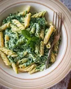 Pasta served in a creamy spinach sauce garnished with fresh herbs