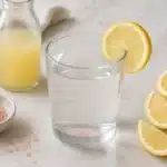Finished pink salt lemon water in a clear glass with lemon and salt nearby